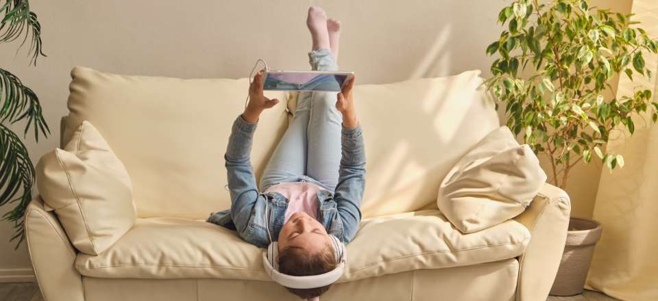 Menina deitadano sofá mexendo no tablet e com fones de ouvido